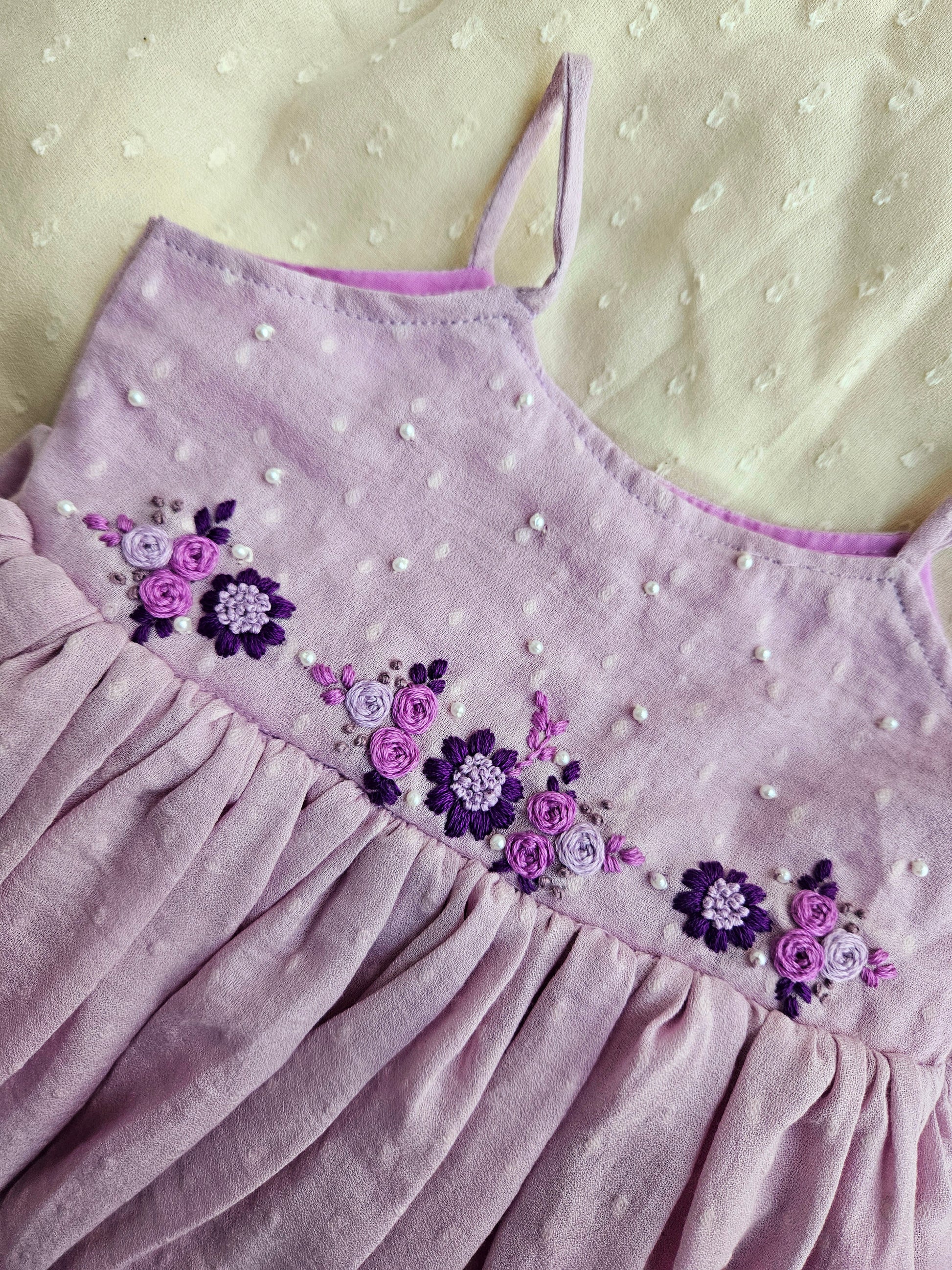 Close-up of purple floral embroidery and pearl details on moss cotton.