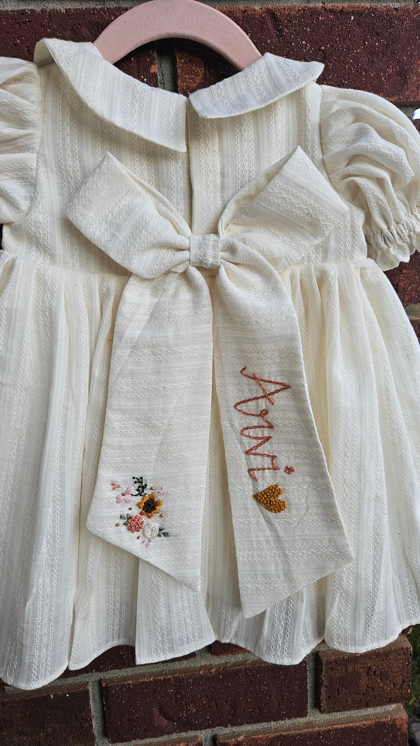 “Ivory kids dress with personalised embroidered bow and floral detailing – sustainable kidswear”
