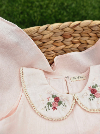 A baby pink cotton linen A-line dress for girls featuring a hand-embroidered Peter Pan collar with delicate pink floral embroidery and scalloped trim. The sleeveless dress has a classic silhouette, making it perfect for birthdays, festive occasions, family outings, and special celebrations.