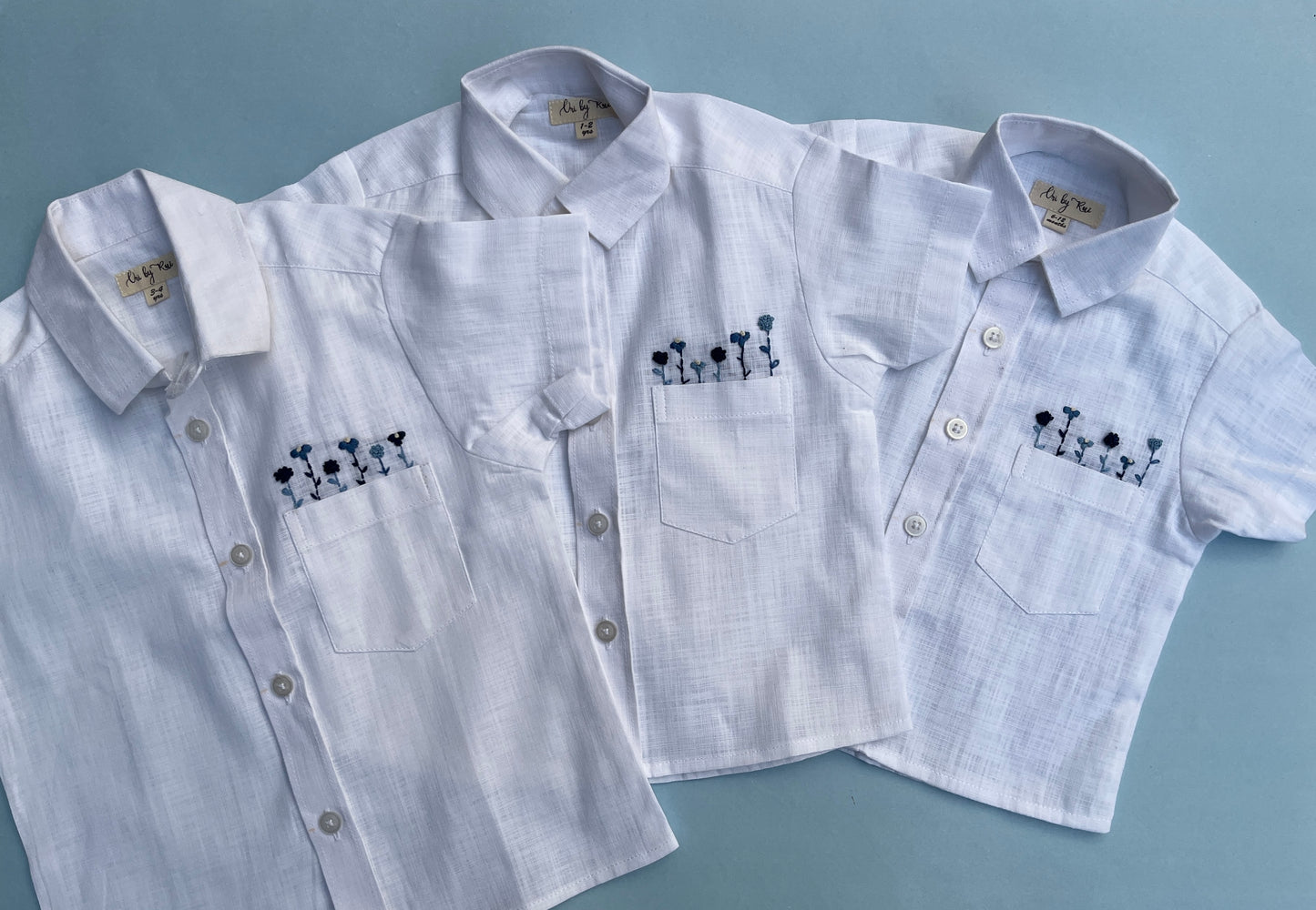 Close-up of hand-embroidered floral pocket on white cotton-linen boys’ shirt.