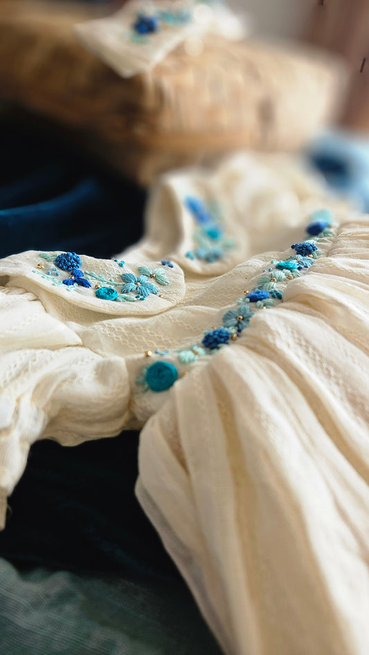 Close-up of blue floral hand embroidery on ivory kids dress