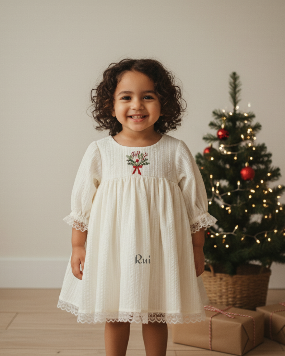 Little girl wearing ivory hand-embroidered Christmas dress standing near tree – Rui.cares